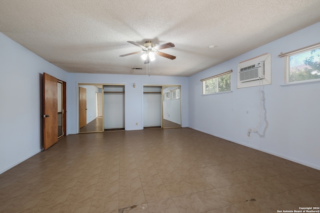 unfurnished bedroom featuring a textured ceiling, two closets, an AC wall unit, and ceiling fan