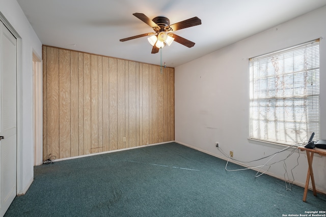 carpeted spare room with ceiling fan, plenty of natural light, and wood walls