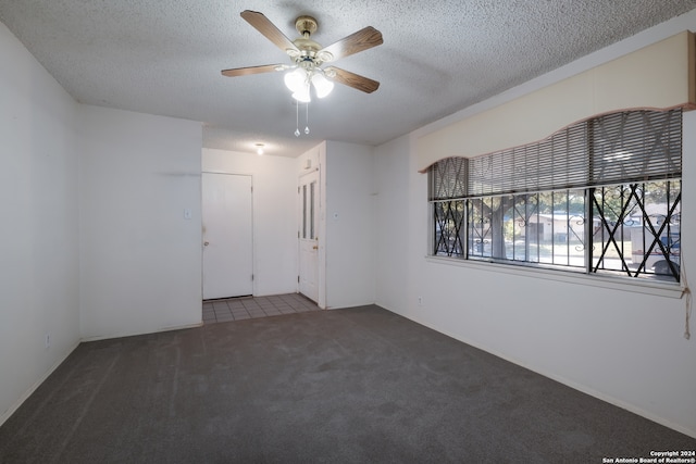 empty room with dark colored carpet, ceiling fan, and a textured ceiling