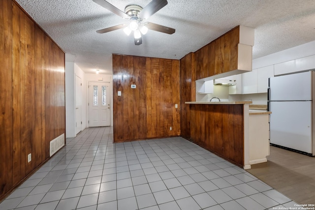 3947 Gayle Ave, San Antonio, TX 78223 - kitchen with freestanding refrigerator, a textured ceiling, ceiling fan, a peninsula, and wooden walls