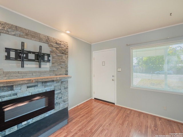 living room featuring hardwood / wood-style flooring, a stone fireplace, and crown molding