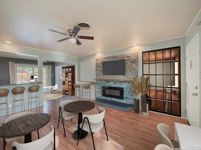 living room featuring a stone fireplace, ceiling fan, crown molding, and light hardwood / wood-style floors