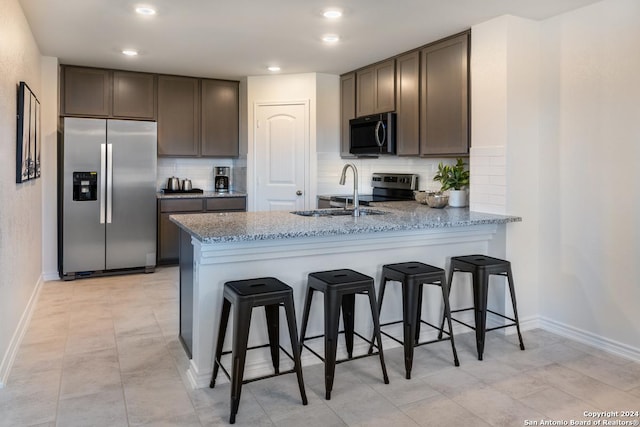 kitchen with sink, a kitchen bar, kitchen peninsula, stainless steel appliances, and light stone countertops