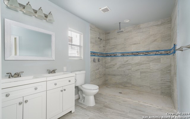 bathroom featuring a tile shower, vanity, and toilet