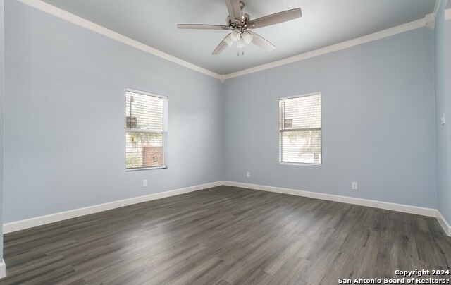 unfurnished room featuring ceiling fan, plenty of natural light, dark wood-type flooring, and ornamental molding