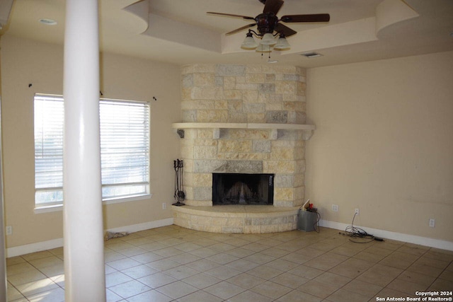 unfurnished living room with a fireplace, light tile patterned floors, a tray ceiling, and ceiling fan