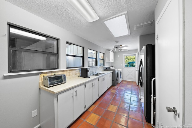 kitchen featuring decorative backsplash, a skylight, ceiling fan, washing machine and clothes dryer, and white cabinetry