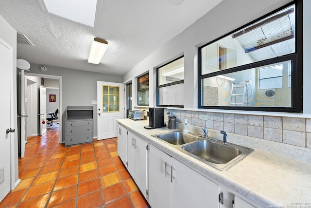 kitchen featuring sink, light tile patterned floors, a textured ceiling, tasteful backsplash, and white cabinetry