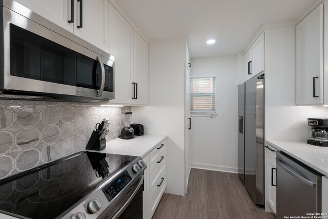 kitchen with light hardwood / wood-style flooring, decorative backsplash, light stone countertops, appliances with stainless steel finishes, and white cabinetry