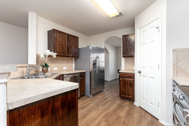 kitchen with backsplash, dark brown cabinets, stainless steel appliances, sink, and light hardwood / wood-style flooring