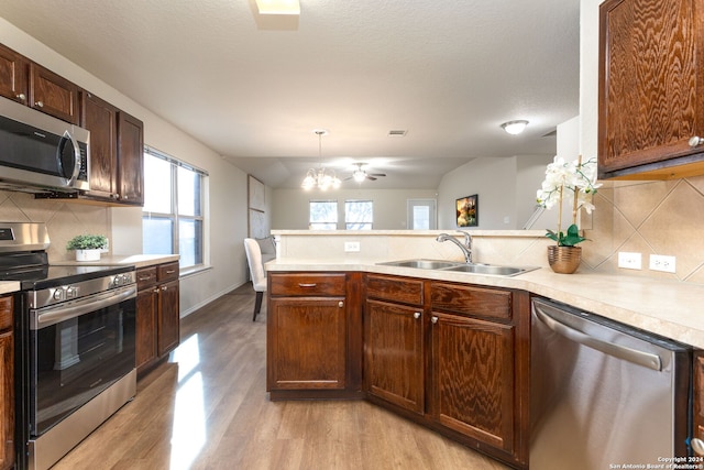 kitchen featuring sink, stainless steel appliances, pendant lighting, light hardwood / wood-style floors, and decorative backsplash