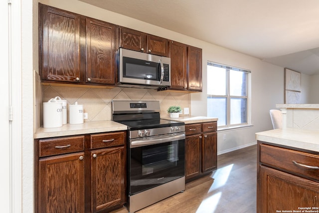 kitchen with tasteful backsplash, dark brown cabinets, stainless steel appliances, and wood-type flooring