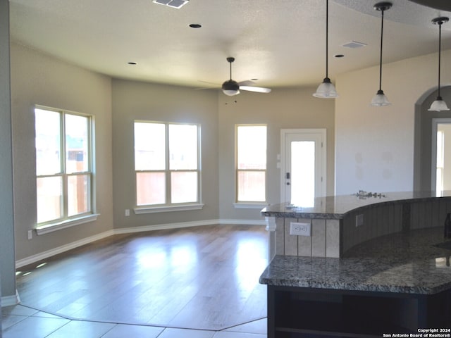 kitchen with dark stone countertops, ceiling fan, decorative light fixtures, and a wealth of natural light