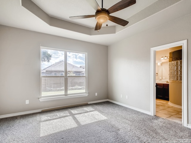 carpeted spare room featuring a tray ceiling and ceiling fan