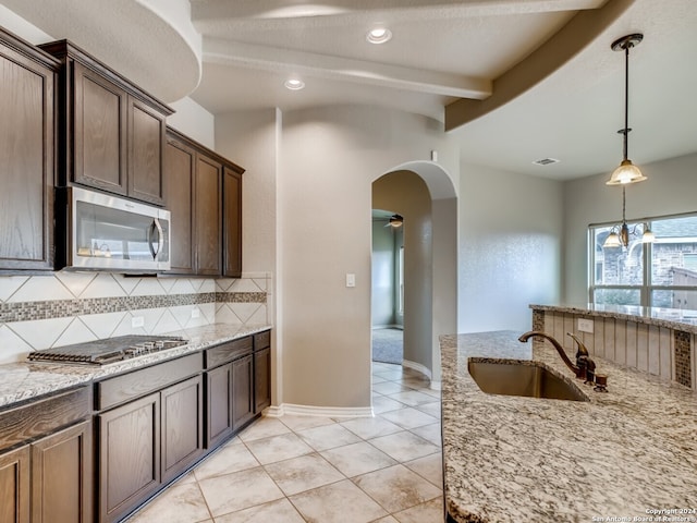 kitchen with appliances with stainless steel finishes, backsplash, light stone counters, sink, and decorative light fixtures