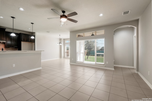 unfurnished living room featuring ceiling fan with notable chandelier, light tile patterned flooring, and a textured ceiling