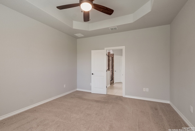 carpeted spare room with a tray ceiling and ceiling fan