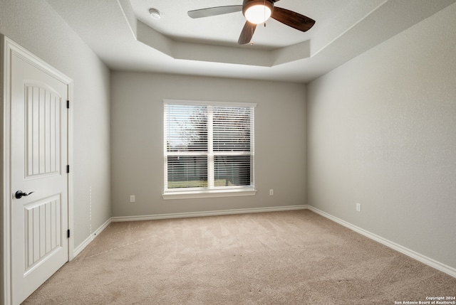 empty room featuring ceiling fan, a raised ceiling, and light carpet