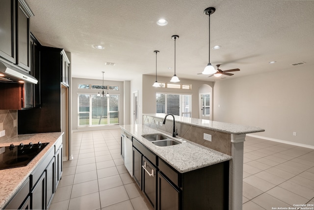 kitchen featuring tasteful backsplash, ceiling fan with notable chandelier, black electric cooktop, a kitchen island with sink, and sink