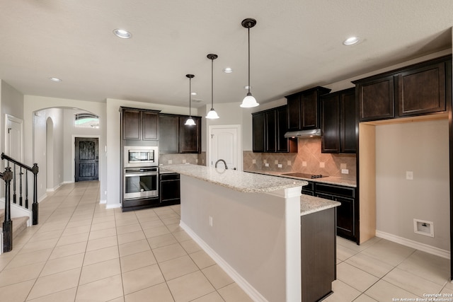 kitchen with a center island with sink, decorative backsplash, light stone counters, and appliances with stainless steel finishes