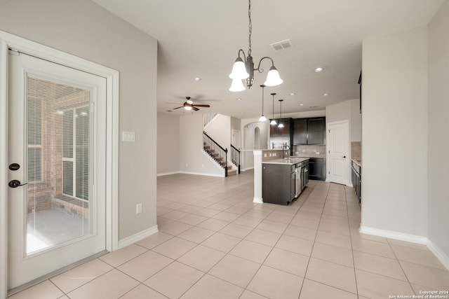 kitchen with hanging light fixtures, ceiling fan with notable chandelier, a kitchen island with sink, and light tile patterned flooring