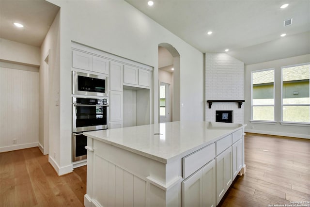 kitchen with stainless steel appliances, light wood-type flooring, a fireplace, a kitchen island, and white cabinets