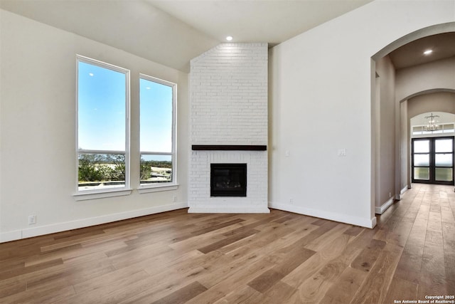 334 Dulce Vis, Boerne, TX 78006 - unfurnished living room with arched walkways, wood finished floors, a brick fireplace, lofted ceiling, and baseboards