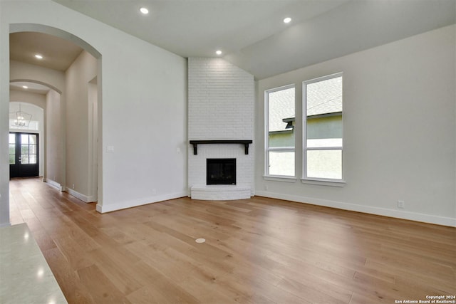 unfurnished living room featuring vaulted ceiling, a brick fireplace, french doors, and light hardwood / wood-style flooring