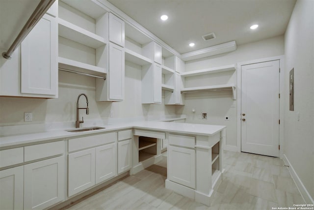 kitchen with electric panel, white cabinetry, and sink