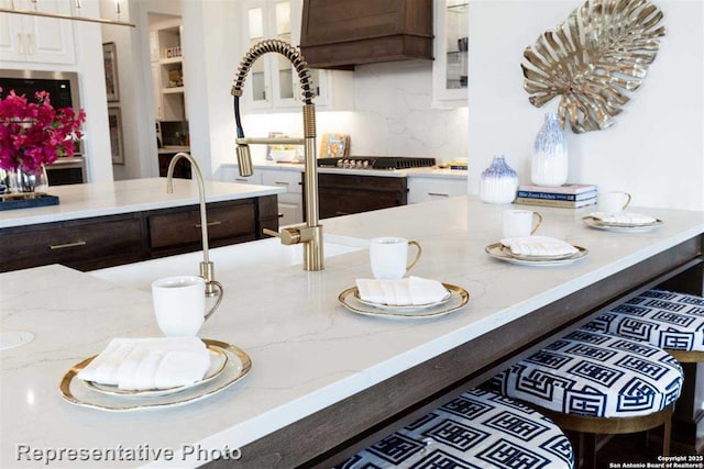 kitchen featuring white cabinetry, light stone countertops, backsplash, and dark brown cabinets