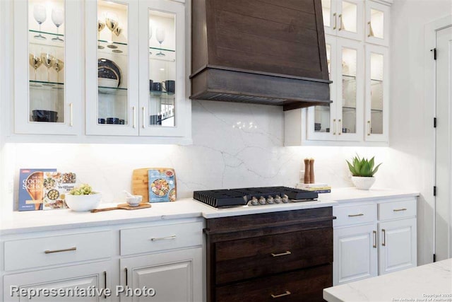 kitchen featuring decorative backsplash, premium range hood, white cabinets, and stainless steel gas cooktop