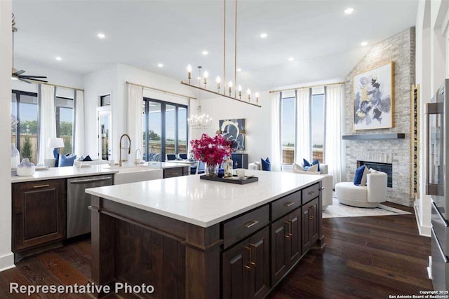 kitchen featuring decorative light fixtures, a brick fireplace, dark hardwood / wood-style floors, dishwasher, and a center island with sink