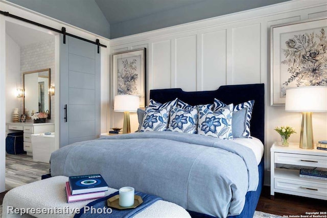 bedroom with ensuite bathroom, a barn door, vaulted ceiling, and dark hardwood / wood-style floors