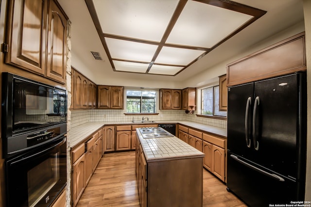 kitchen with black appliances, tile counters, a kitchen island, and light hardwood / wood-style flooring