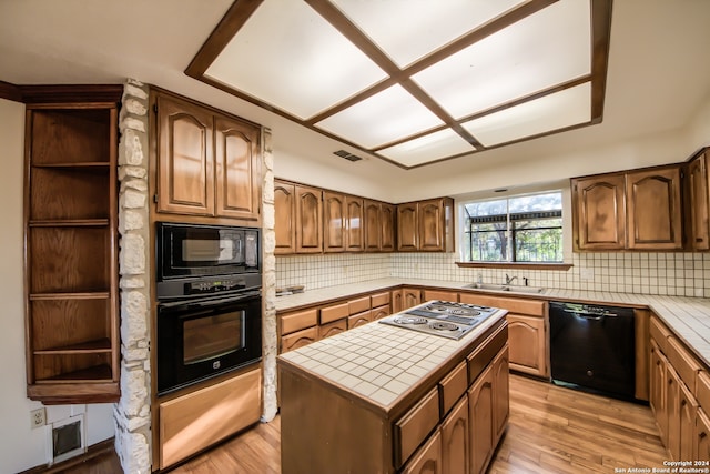 kitchen featuring backsplash, black appliances, tile countertops, light hardwood / wood-style flooring, and a center island