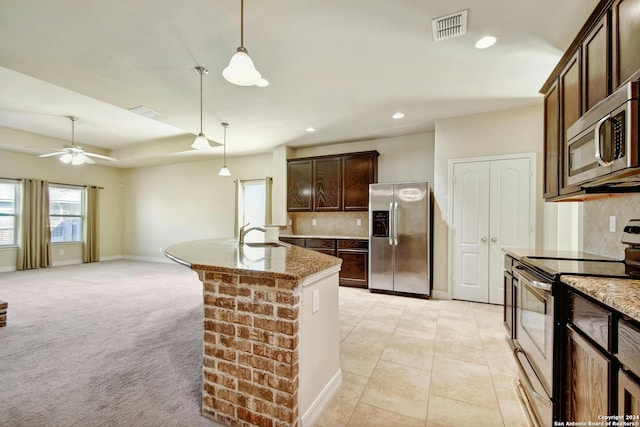 kitchen with a center island with sink, decorative light fixtures, light colored carpet, dark brown cabinetry, and stainless steel appliances