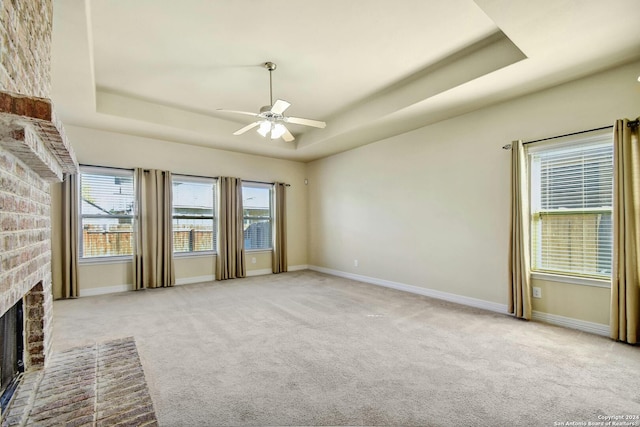 unfurnished living room featuring light carpet, a tray ceiling, and a brick fireplace