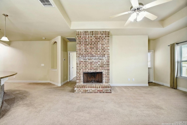 unfurnished living room with light carpet, a tray ceiling, a brick fireplace, and ceiling fan