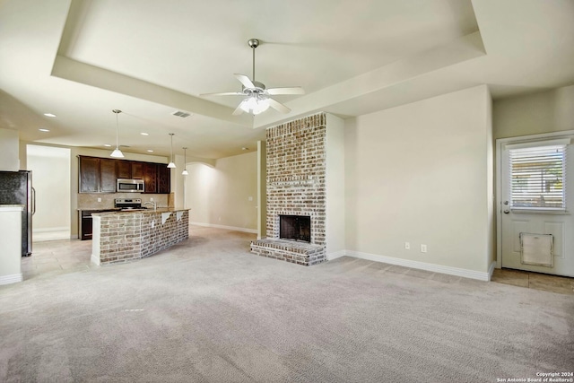 unfurnished living room with a fireplace, light carpet, a raised ceiling, and ceiling fan