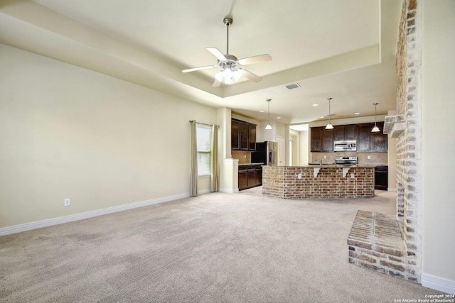 unfurnished living room featuring a raised ceiling, ceiling fan, and light colored carpet