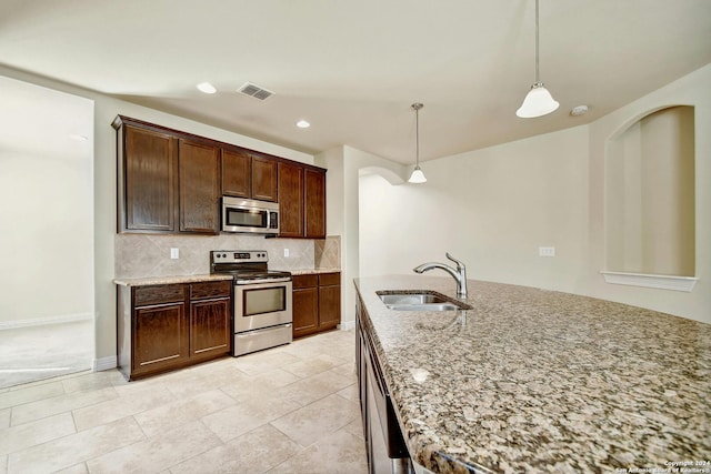 kitchen with light stone countertops, appliances with stainless steel finishes, backsplash, sink, and hanging light fixtures