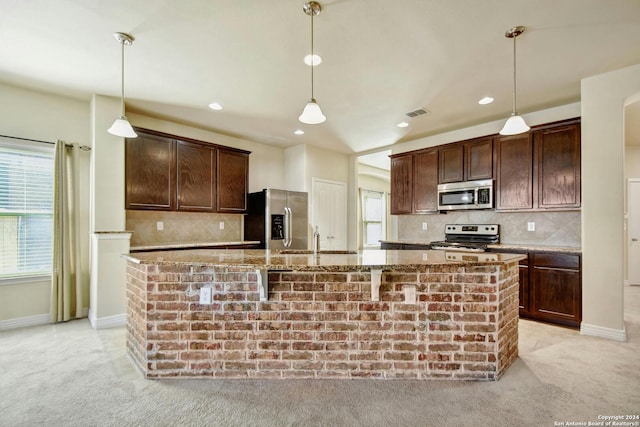 kitchen with a center island with sink, a healthy amount of sunlight, stainless steel appliances, and pendant lighting