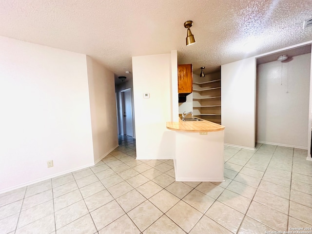 kitchen featuring sink, light tile patterned flooring, a textured ceiling, and wood counters