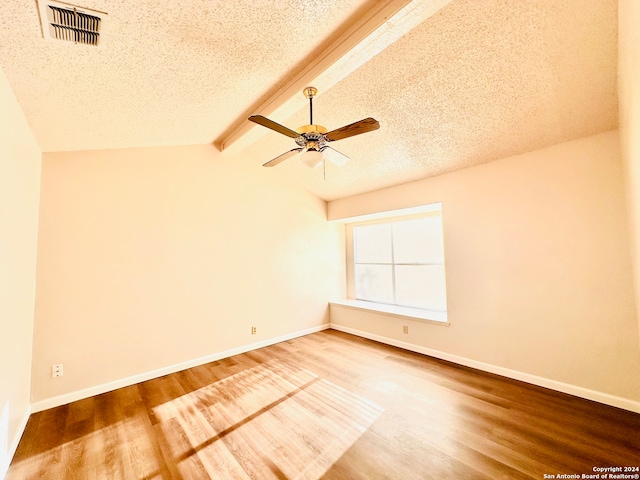 empty room with ceiling fan, lofted ceiling with beams, a textured ceiling, and hardwood / wood-style flooring