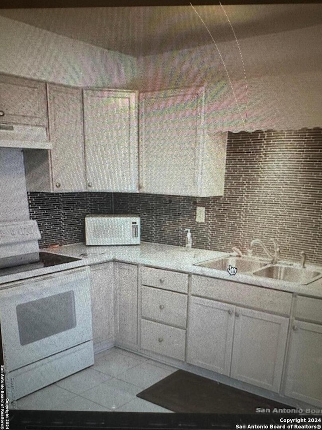 kitchen with backsplash, sink, light tile patterned floors, oven, and white cabinetry