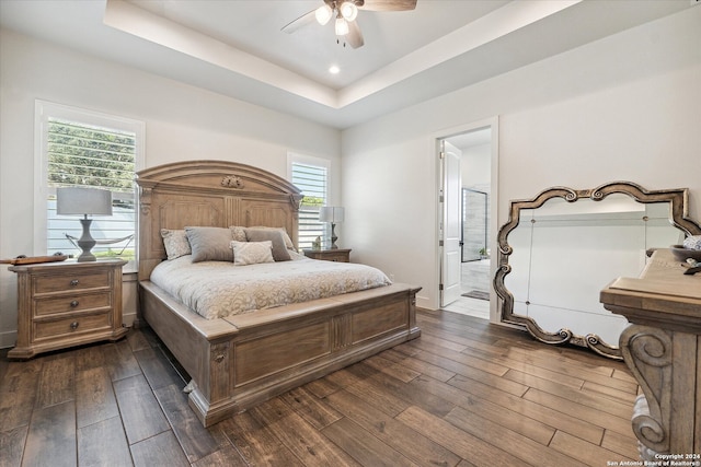 bedroom featuring dark hardwood / wood-style floors, ceiling fan, a raised ceiling, and ensuite bathroom