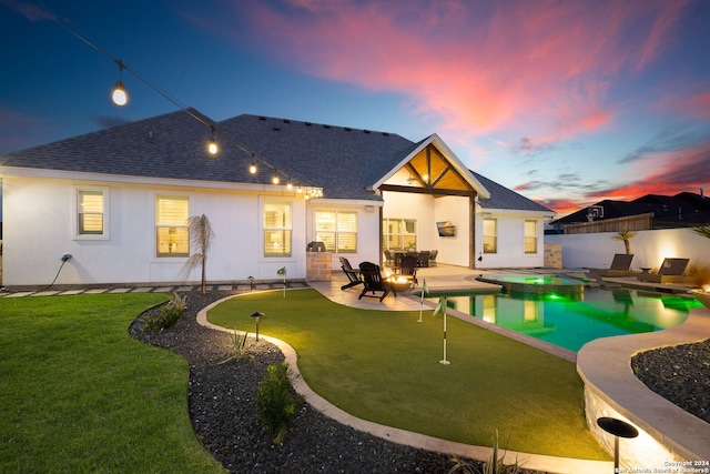 back house at dusk featuring a swimming pool with hot tub, a patio, and a lawn