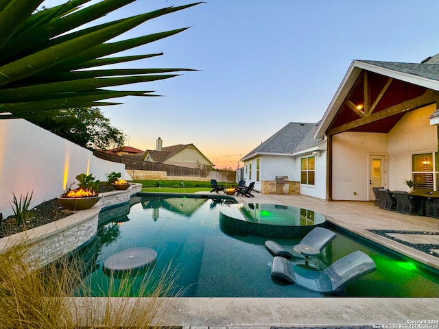 pool at dusk with area for grilling and a patio