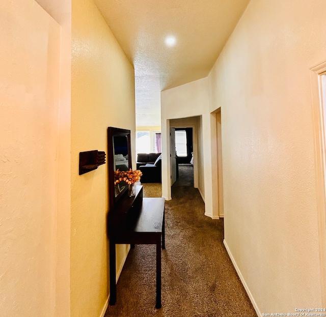 corridor featuring a textured ceiling and dark colored carpet