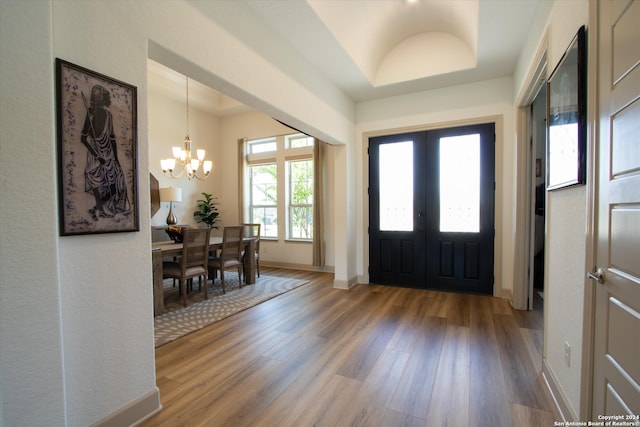 foyer with wood-type flooring, a tray ceiling, french doors, and a notable chandelier